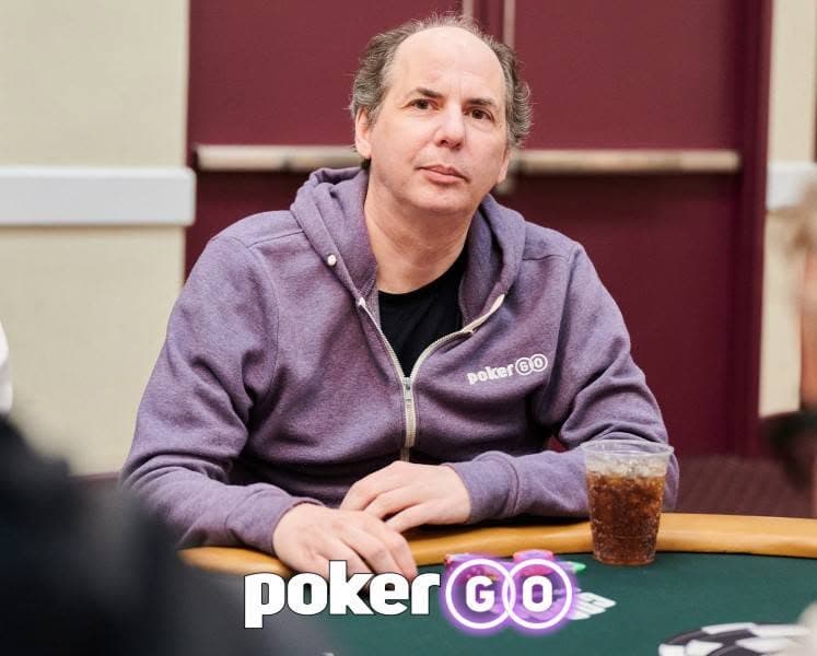 Allen Kessler seated at a green felt poker table wearing a purple PokerGO hoodie